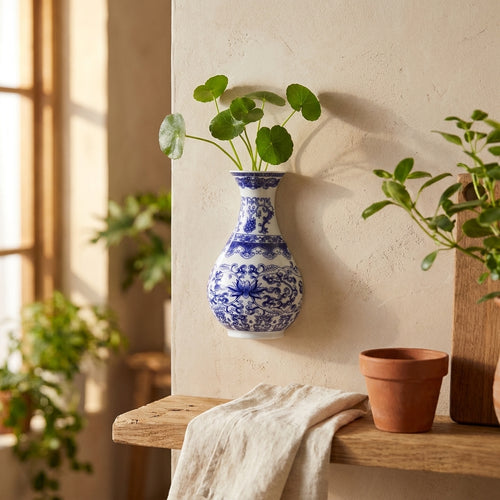 Blue and white porcelain wall vase with green cuttings on a plaster wall