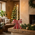 Red striped ceramic bow candle holder with a lit taper on a rustic mantel