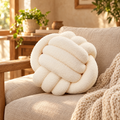Cream knot pillow on a linen armchair with a chunky knit throw
