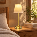 Pleated cordless table lamp glowing on a wooden bedside table