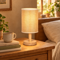 Linen shade table lamp glowing on a wooden bedside table