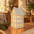 White metal cottage candle holder glowing on a wooden table with pinecones