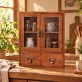 Vintage wood mini cabinet with glass doors holding jars and teacups on a kitchen counter