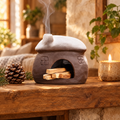 Ceramic cottage incense burner with snowy roof and palo santo on a wooden mantel