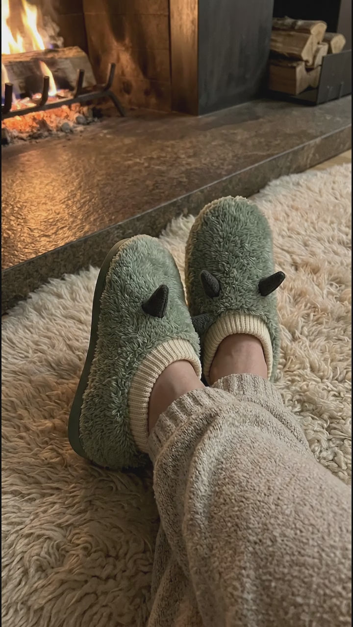 Feet in green heated plush slippers by a cozy fireplace